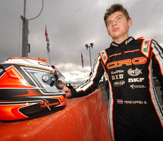 Person in racing suit with helmet on a podium at a race track
